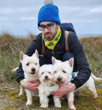 Een man knuffelt zijn drie honden die Kenzo, Kwinto en Buddy heten.